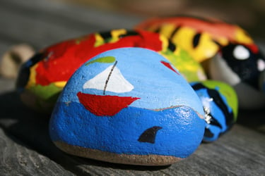 A Kindness Rock painted with a boat scene in front of other rocks. 